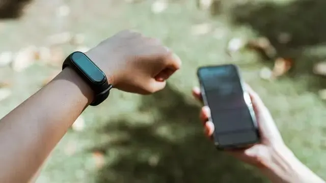 Een pols met een zwarte smartwatch en een hand met een zwarte smartphone tegen een groene achtergrond.