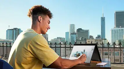 Een laptop op een bruine tafel met een smartphone. Op de achtergrond een stadsgezicht met hoge gebouwen tegen een blauwe hemel.