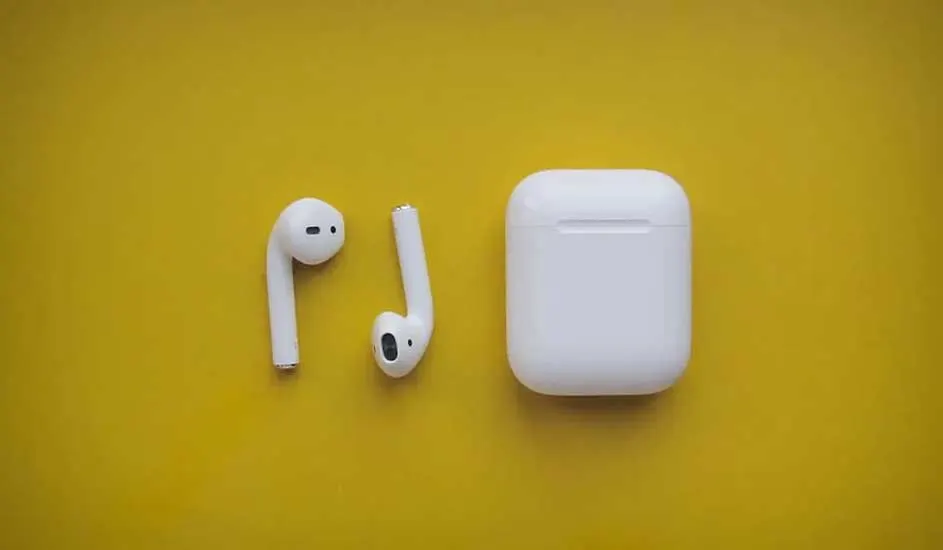 Two white wireless earbuds and their rectangular charging case are neatly arranged on a flat yellow background, creating a grafische compositie.