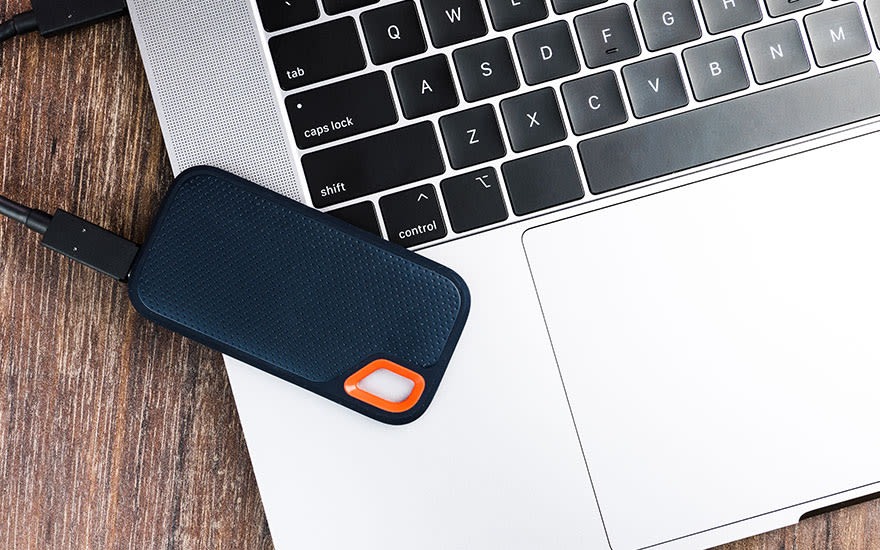 Un disque dur bleu est connecté à un ordinateur portable blanc sur une table en bois. Le clavier est noir et argenté.