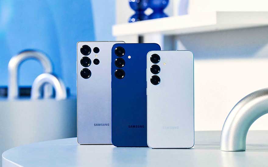 Drie Samsung-smartphones staan op een ronde tafel in een lichte keuken; zilver, donkerblauw en wit, met meerdere camera’s achteraan.