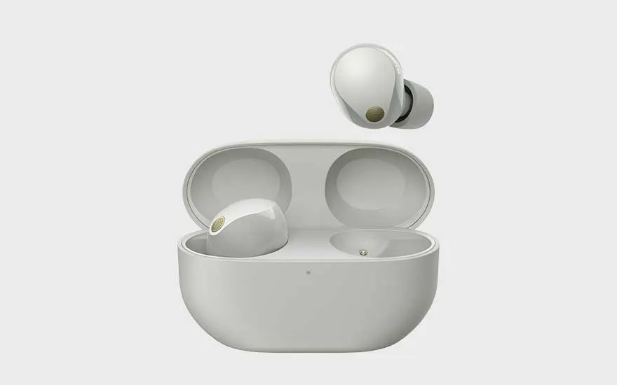 Elegant white wireless earbuds with gold accent sit in a premium charging case, one earbud hovering above on a pale background.