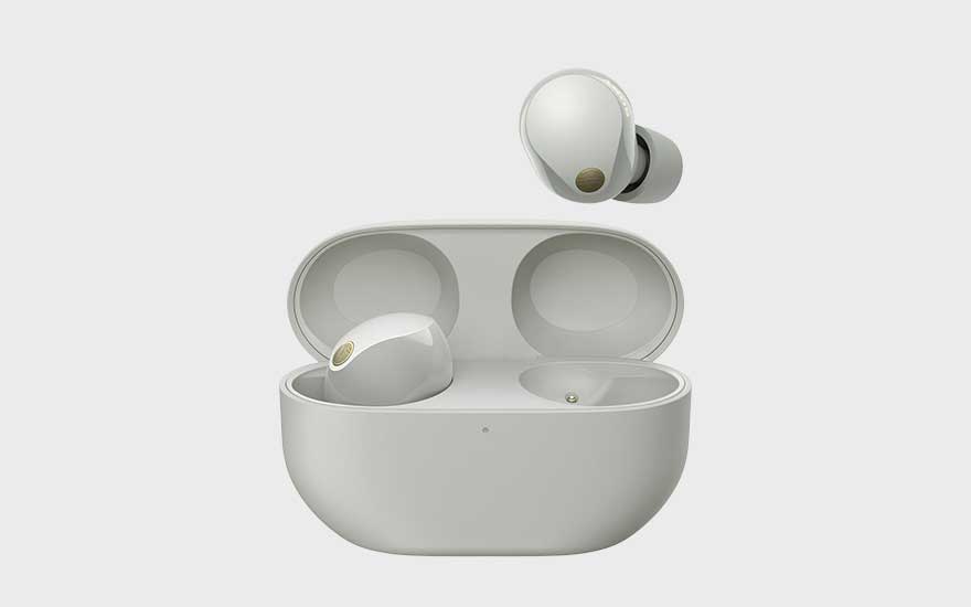 Elegante witte draadloze oordopjes met goudaccent liggen in een luxe oplaadcase, één oordop zweeft erboven op lichte achtergrond.