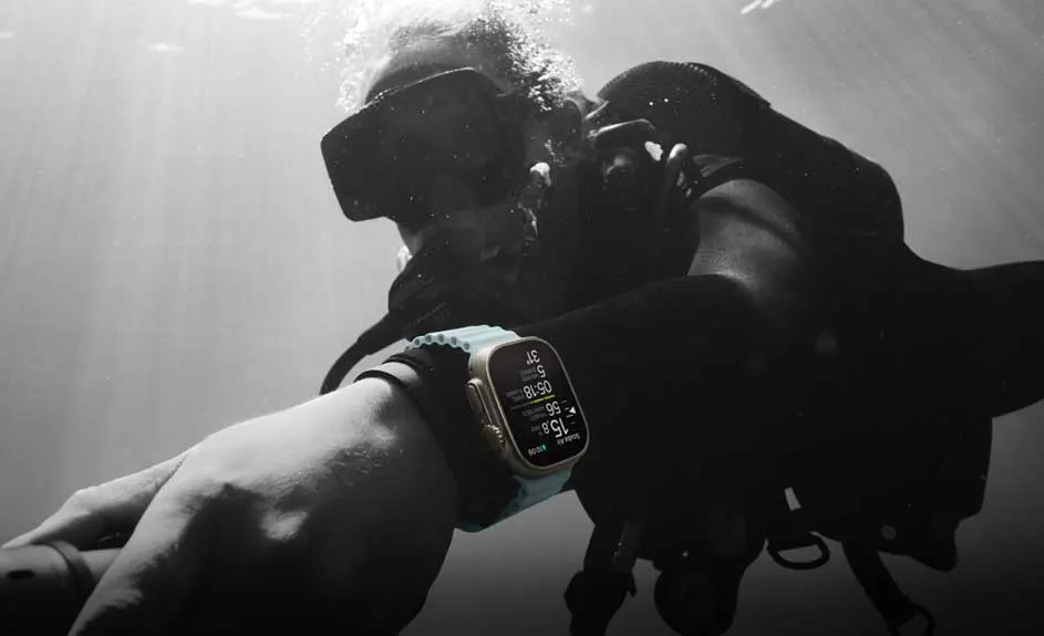 Un plongeur porte une montre dorée avec un bracelet bleu sous l'eau, l'écran affiche des données.