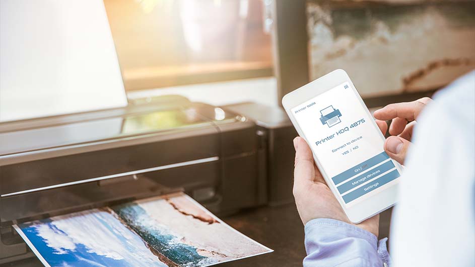 Une imprimante noire imprime une photo. Un smartphone affiche une application d'imprimante.