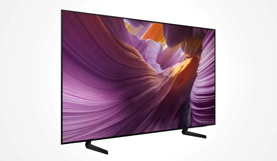 Een Samsung televisie met dun zwart frame toont een kleurrijk beeld van een paarse canyon met zonlicht, geplaatst op twee slanke pootjes.