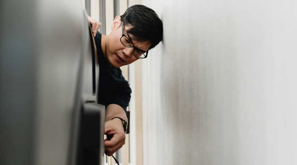 Un homme en lunettes connecte un câble à un appareil gris près d'un mur blanc.