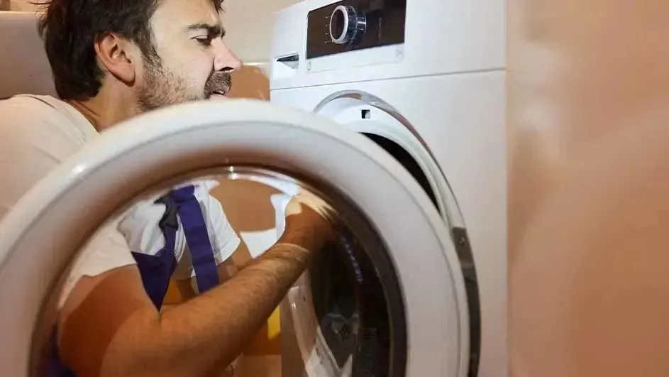 Een witte wasmachine met open deur, naast een beige muur.