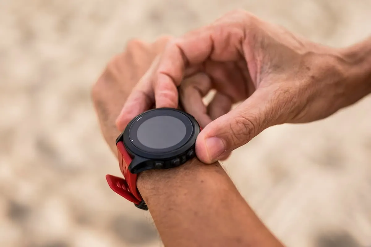 Imagen primer plano de una muñeca de hombre con un reloj deportivo con la esfera redonda y de color negro, con la correa de silicona de color rojo.