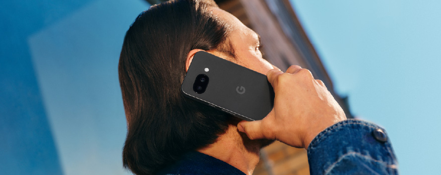 Mujer en un coche, con chaqueta azul, hablando por teléfono negro con la mano levantada.