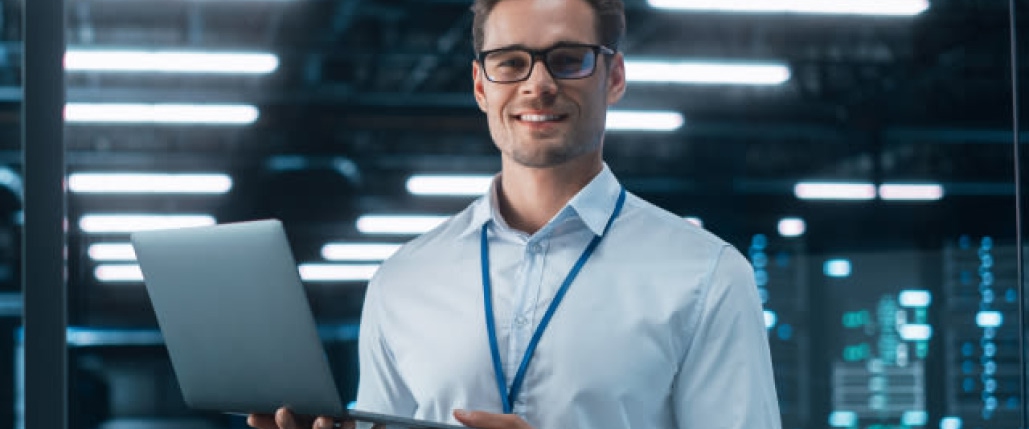 Un hombre con gafas sostiene un ordenador portátil en un centro de datos rojo. Texto en blanco: "DETECTAR fraudes y aumentar la protección".