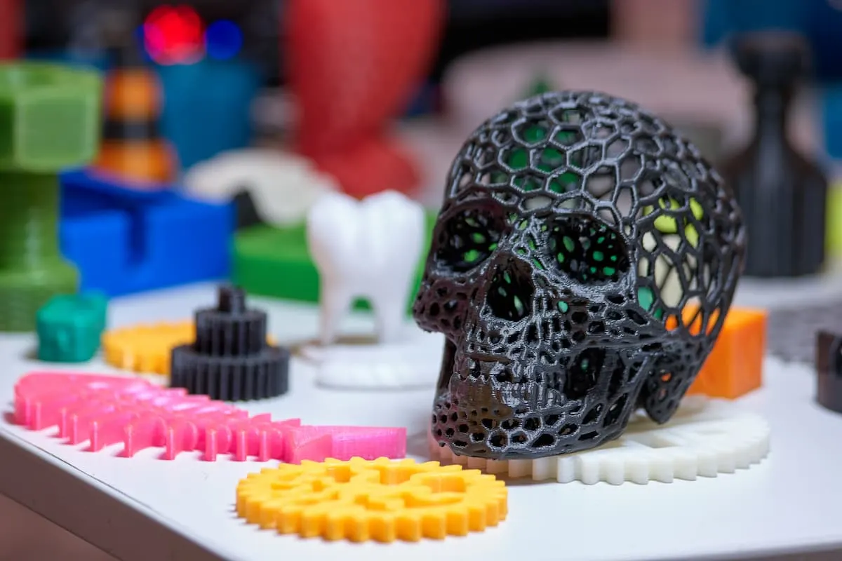Calavera negra de estructura geométrica impresa en 3D junto a varias piezas de colores sobre una mesa.