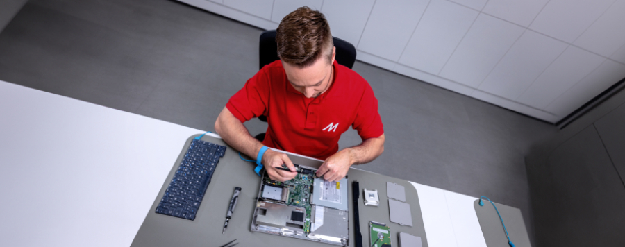 Técnico con uniforme MediaMarkt limpiando interior de portátil, manipulando placa base y componentes electrónicos