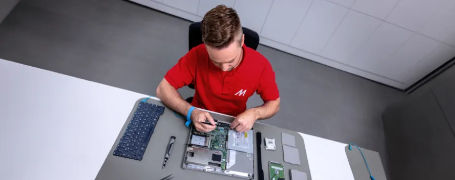 Técnico con uniforme MediaMarkt limpiando interior de portátil, manipulando placa base y componentes electrónicos