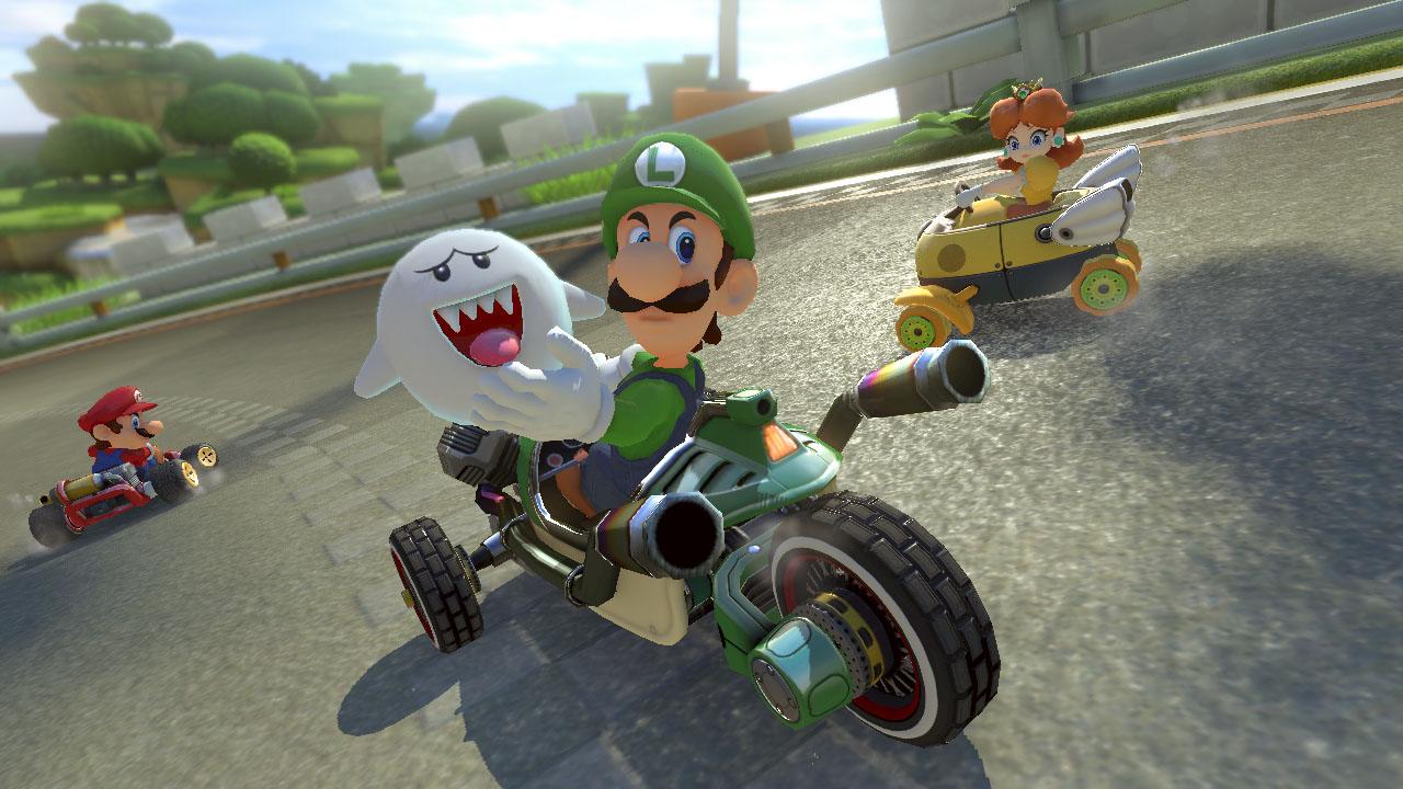 Luigi en moto verde con Boo. Mario en kart rojo a la izquierda y Daisy en vehículo amarillo a la derecha, en pista gris.