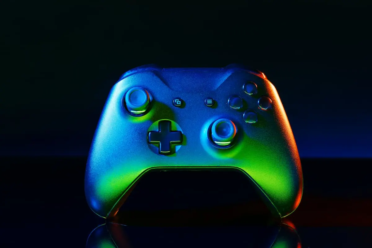 Mando de videojuegos iluminado con luces verdes y azules sobre fondo oscuro.
