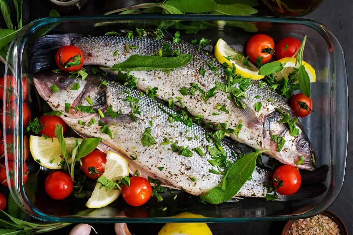 dos lubinas crudas en una fuente para horno con especias en una mesa negra