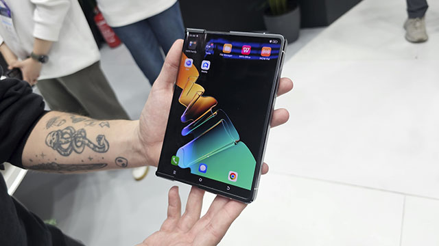 Una persona sostiene un móvil con una pantalla que muestra un fondo abstracto con tonos verdes, naranjas y azules.