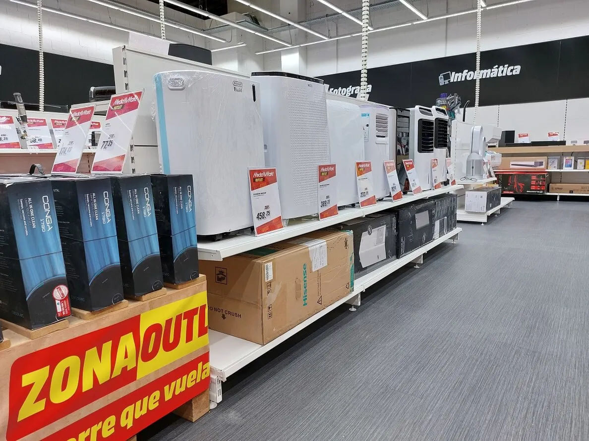 Estanterías blancas exhiben purificadores de aire, cajas de cartón y electrodomésticos en una tienda con letrero de "Informática".
