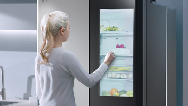 Persona tocando la puerta de vidrio de un refrigerador para ver el interior.