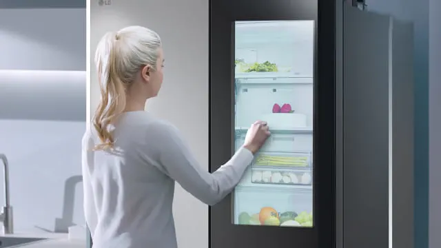 Persona tocando la puerta de vidrio de un refrigerador para ver el interior.