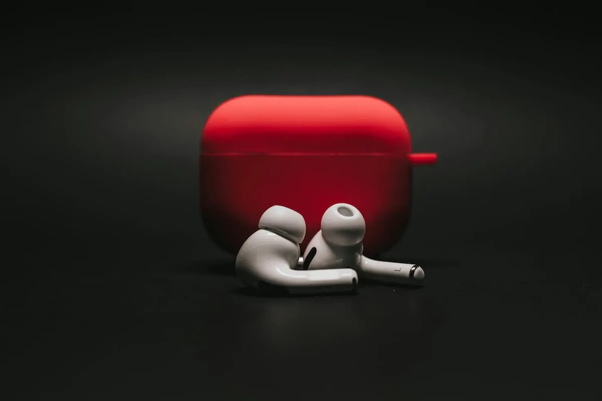 Auriculares inalámbricos blancos con estuche rojo sobre fondo negro.