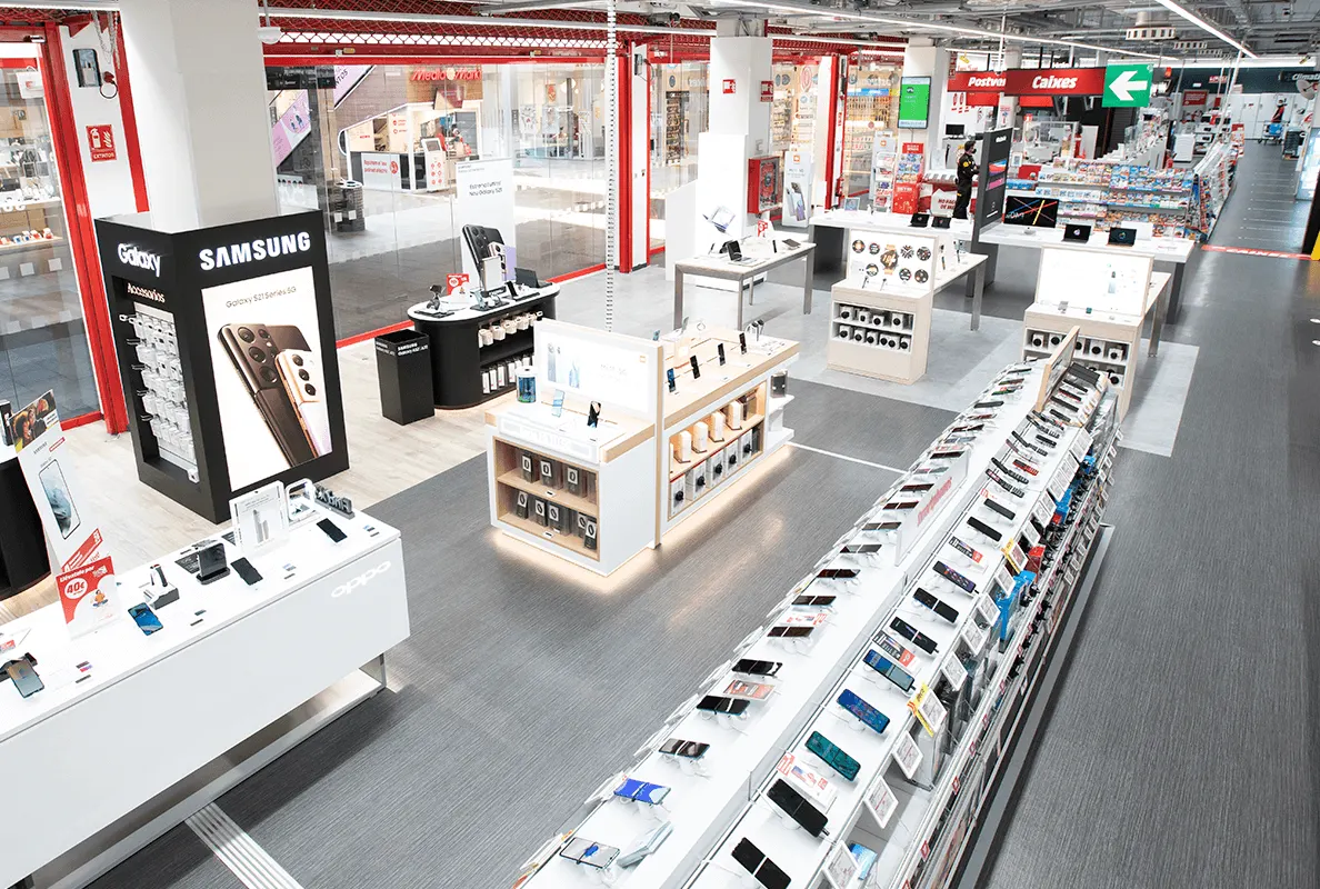 Interior de tienda de electrónica con estantes y expositores de móviles y accesorios, con señalización en el techo.