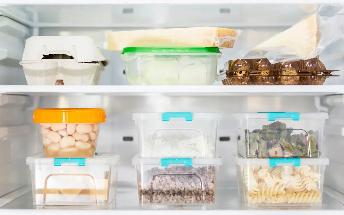 Un refrigerador blanco contiene comida en recipientes: huevos, queso, frijoles, arroz, carne molida, espárragos y pasta.