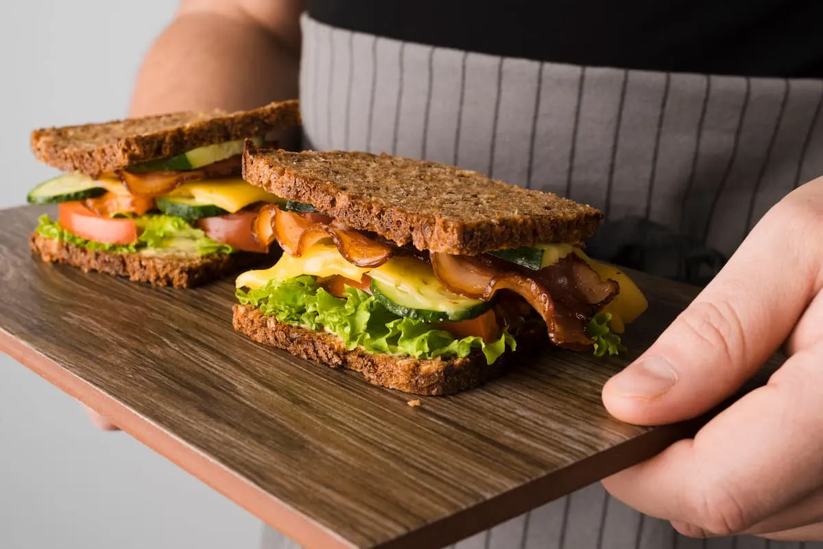 Persona sosteniendo una tabla con dos sándwiches de pan integral.