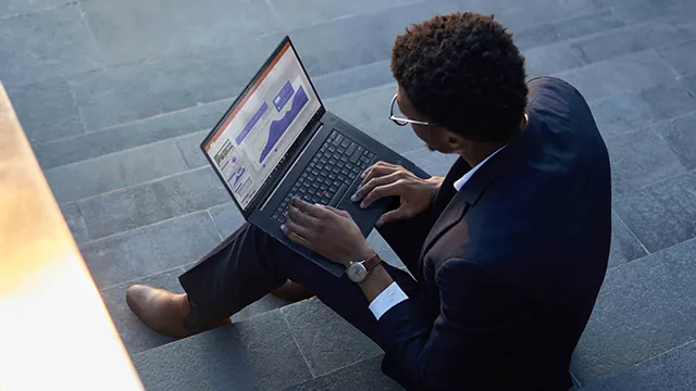 Un hombre con traje usa una laptop con gráficos mientras está sentado en escaleras grises. Lleva un reloj plateado.
