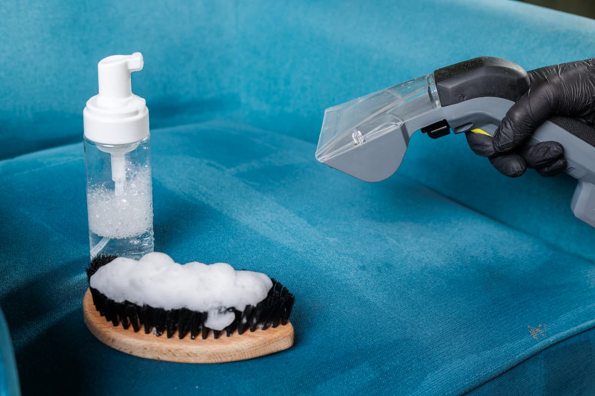 Cepillo con espuma y limpiatapicerías sobre un sofá azul.