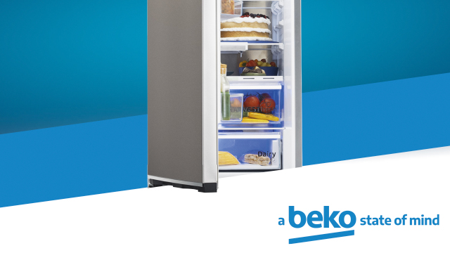 Un refrigerador gris abierto muestra estantes con tarta, fruta, verduras, queso y embutidos sobre un fondo azul.