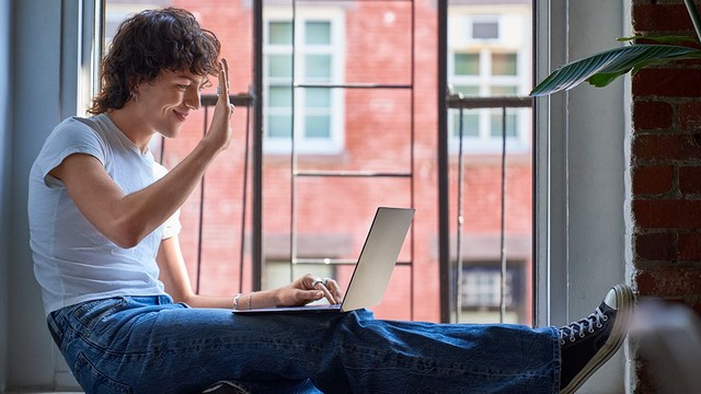 Persona sentada en una venta que saluda a través de un portátil.