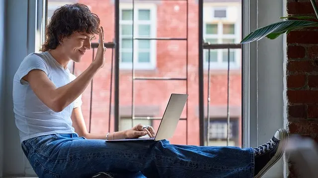 Persona sentada en una venta que saluda a través de un portátil.