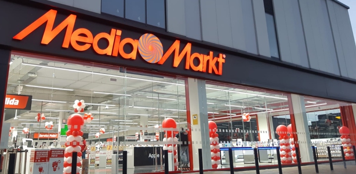 Fachada de tienda Media Markt con letrero naranja y decoración de globos rojos y blancos en la entrada.