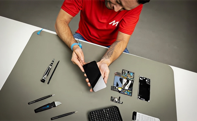 Hombre reparando un teléfono con una camiseta roja de MediaMarkt