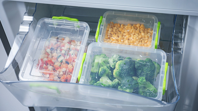 Cajón de nevera abierto con tres recipientes de plástico: uno con verdura picada, otro con garbanzos y el último con brócoli.