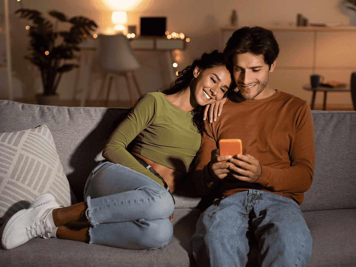 Pareja sentada en un sofá usando un smartphone.