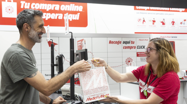 En una tienda, un hombre recibe una bolsa de una empleada detrás de un mostrador con letreros en español.