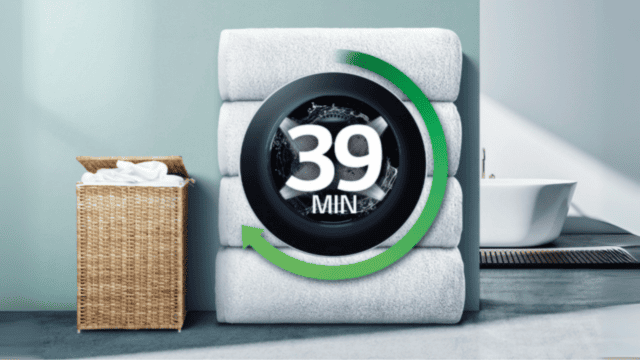 Lavadora LG con ciclo rápido de 39 minutos, sobre toallas apiladas junto a un cesto de ropa.