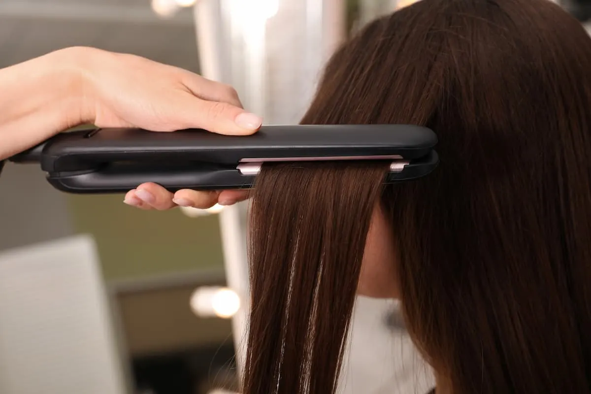 Mano usando una plancha de pelo negra para alisar el cabello liso de una mujer.