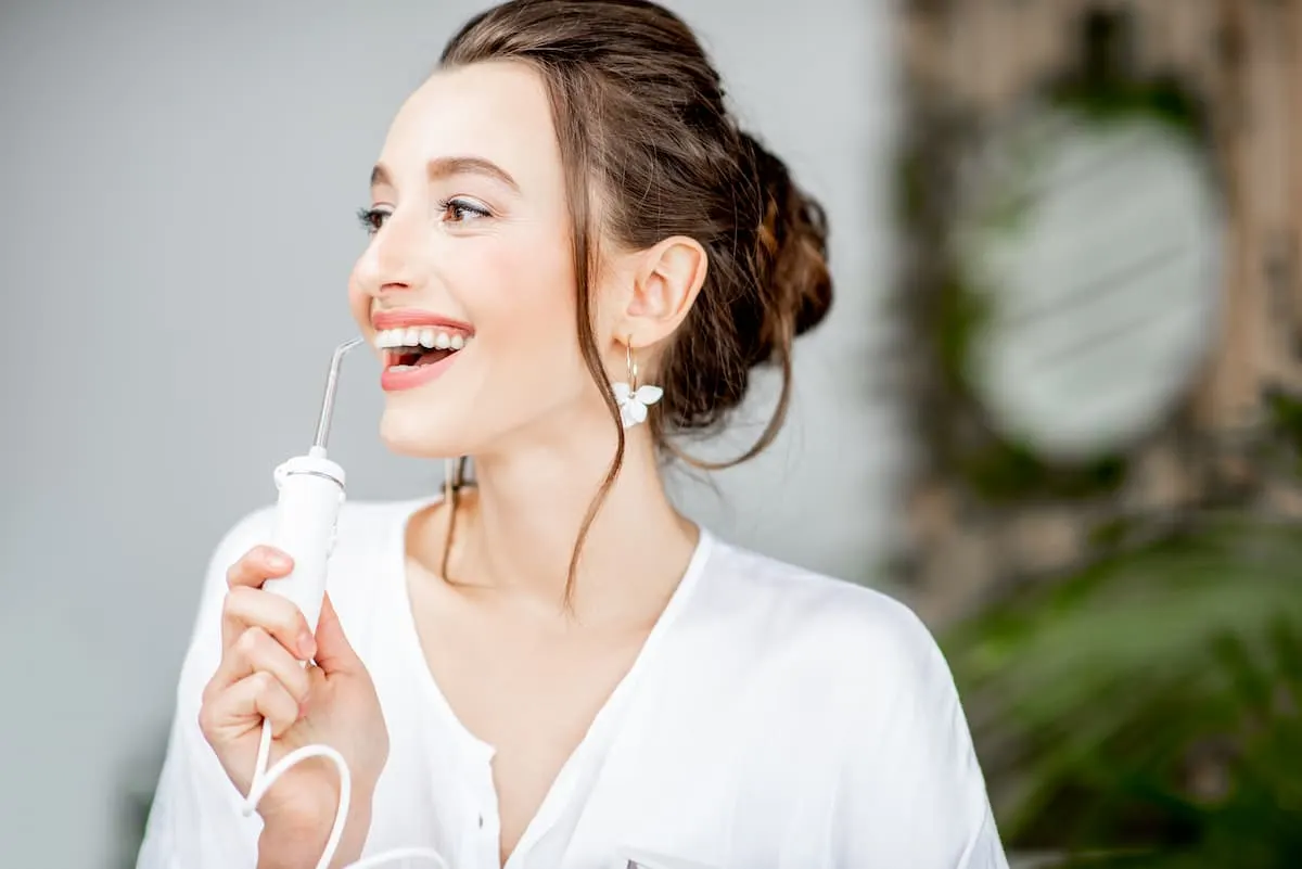 Mujer sonriente usando un irrigador dental blanco.