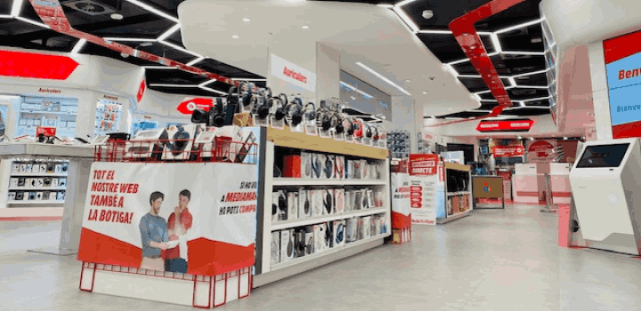 Interior de tienda con estanterías de auriculares y carteles promocionales en rojo y blanco. Un quiosco digital está al fondo.