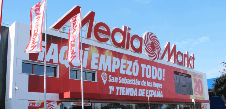 Edificio de Media Markt con letreros rojos y blancos, y banderas ondeando al frente.