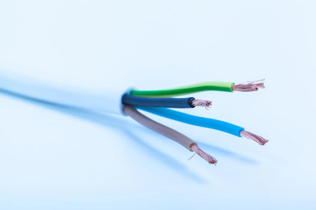 Primer plano de un cable eléctrico pelado con varios hilos de cobre de colores expuestos.