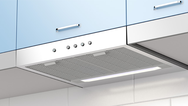 Alacenas azules sobre campana extractora metálica con rejilla y luz blanca. Botones de control visibles en la parte frontal.