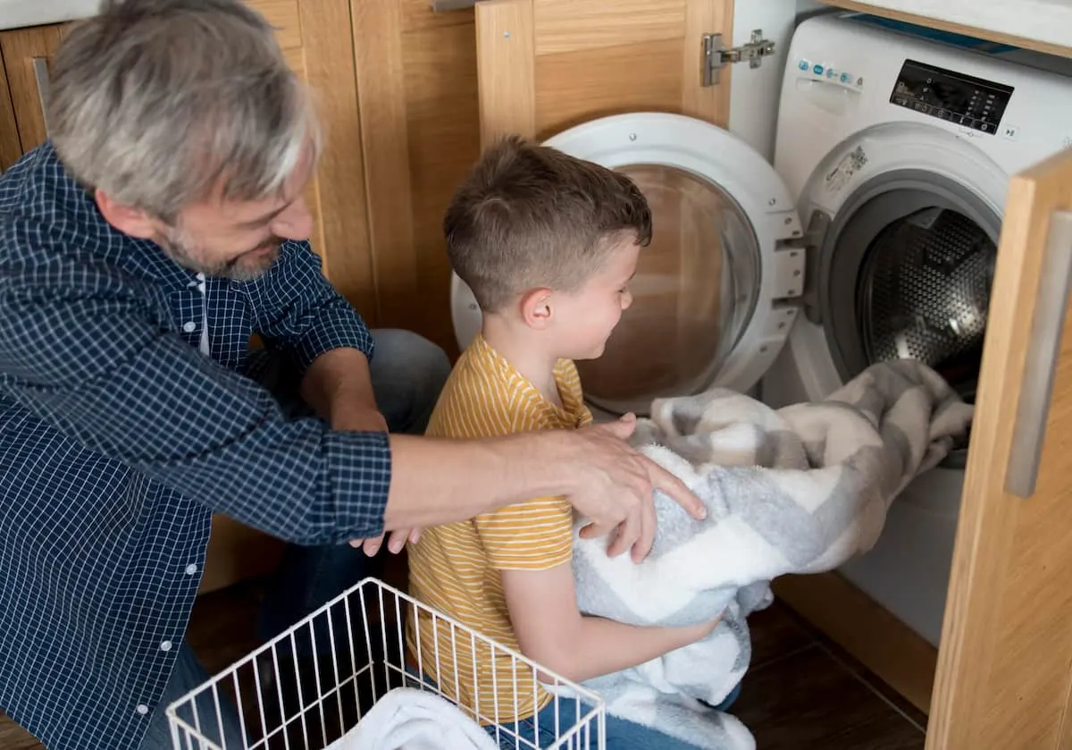 Hombre y niño metiendo ropa en una lavadora secadora.