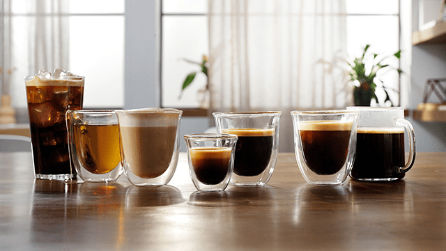 Varias bebidas en vasos de vidrio sobre una mesa de madera, incluyendo café, té helado y otras bebidas calientes.