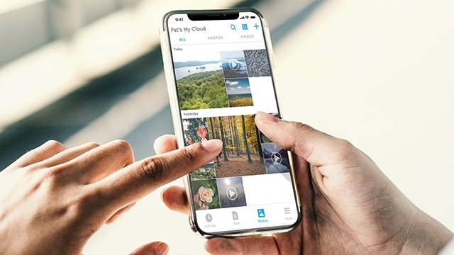 Persona tocando la pantalla de un teléfono móvil que muestra una galería de fotos con iconos y texto.
