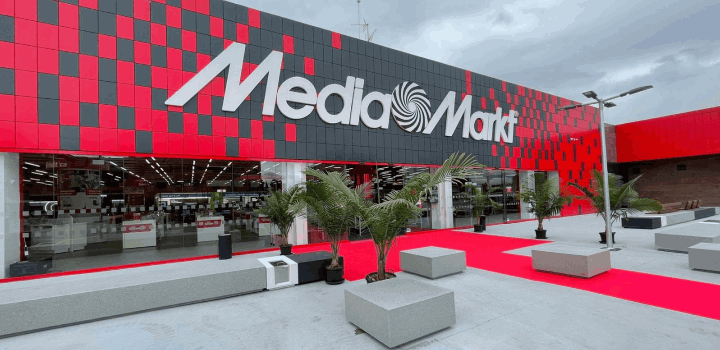 Edificio de Media Markt con fachada roja y gris, logo blanco, plantas ornamentales y asientos grises.
